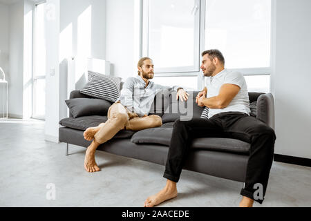 Two male friends having a serious discussion while sitting together on the couch in the living room at home Stock Photo