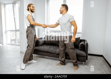 Two happy professional movers or repairmen in workwear shaking hands together, finishing work in the apartment Stock Photo