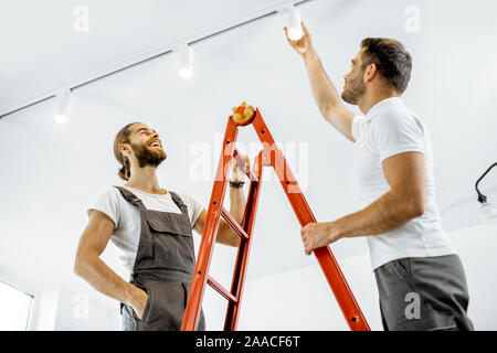 Two repairmen or professional electricians installing light spots, standing on the ladder in the living room of the modern apartment Stock Photo