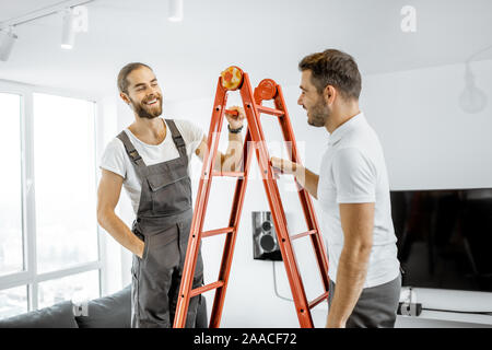 Two handsome workmen in uniform talking on the ladder during some repairment at home Stock Photo