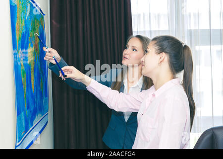 Two business-like young women plot a route on a geographical map for the delivery of cargo. Stock Photo