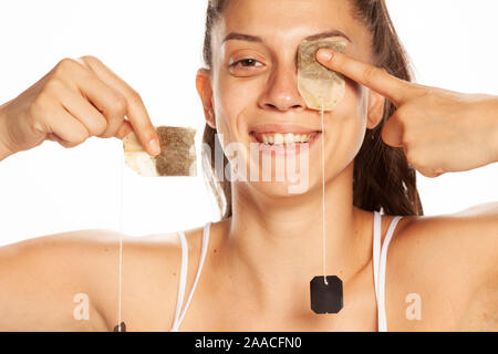 Young smiling woman posing with tea bag on her eye on white background Stock Photo