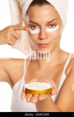 Young woman applying face cream under her eyes on white background Stock Photo