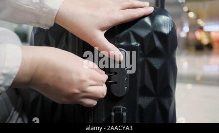 Woman fastens the combination lock on the suitcase in airport. She is preparing to flight in airport, travel concept. Hands closeup. Stock Photo