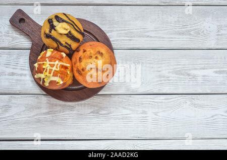 Sweet and tasty snack. Three different colorful cupcakes on a wooden background. Stock Photo