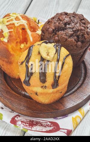 Sweet and tasty snack. Three different colorful cupcakes on a wooden background. Stock Photo