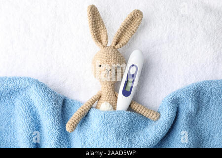 Toy bunny with thermometer on towel background, top view Stock Photo