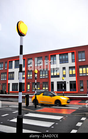 Orange car going over pedestrian crossing in front of school on a wet late afternoon in winter Stock Photo