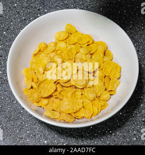 Dry cereal in morning. Cornflakes in white bowl on grey table preparing breakfast. Traditional meal. Stock Photo