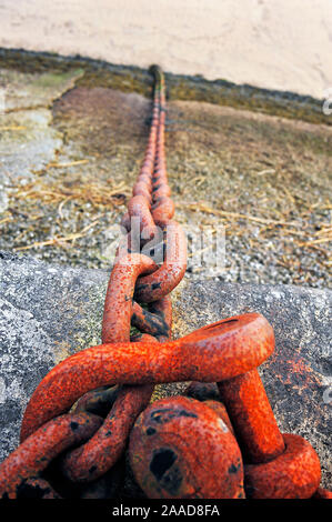 Rusty chain hanging over quayside on to beach below Stock Photo