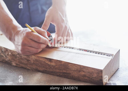 A carpenter in working clothes and a small business owner takes a wooden board with a ruler and pencil. Stock Photo