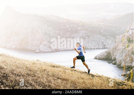 man athlete running uphill on background sea bay in sunset
