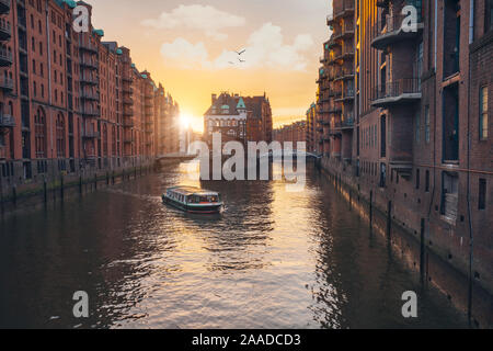 Famous hamburg warehouse district. Water castle palace and tourist boast in river in sunset golden light. Old warehouse port, Germany, Europe. Stock Photo