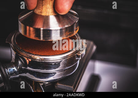 Barista pressing ground coffee into portafilter by tamper to making coffee Stock Photo