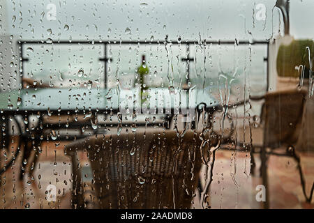 view through a window pane covered with raindrops onto furnished terrace during rainy season in Nerja, Spain Stock Photo