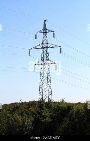 Large power line utility pole made of metal pipes with electrical wires connected with tall; glass insulators rising high above dense forest on clear Stock Photo