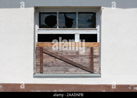 Partially boarded window with broken glass and dilapidated wooden frame at abandoned building of old military complex on warm sunny summer day Stock Photo