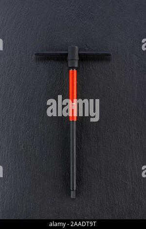 Professional reinforced black matt T-shape wrench placed on a dark background. T-type handle Tool used in a workshop. View from the top. Stock Photo