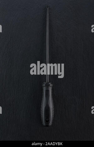 Professional reinforced black matt screw driver placed on a dark ground. View from the top. Stock Photo