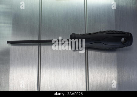 Professional reinforced black matt screw driver placed on a polished aluminum surface. View from the top. Stock Photo