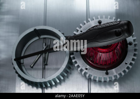 Professional reinforced black matt screw driver placed on a gearwheel. View from the top. Stock Photo