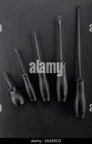 Professional reinforced black matt screw drivers placed on a dark ground. View from the top. Stock Photo