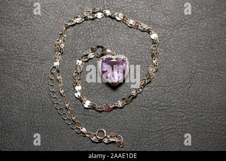 Necklace with heart-shaped pendant on a gold chain. With a gemstone of purple color in gold setting. Decoration for women. Isolated. On a dark backgro Stock Photo