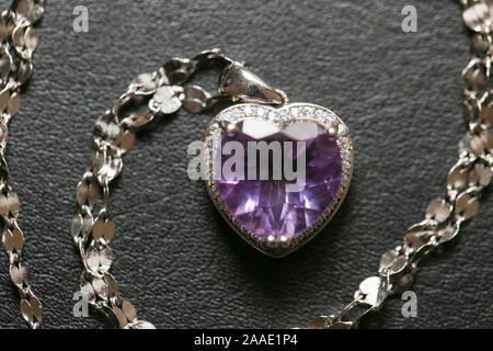 Necklace with heart-shaped pendant on a gold chain. With a gemstone of purple color in gold setting. Decoration for women. Isolated. On a dark backgro Stock Photo