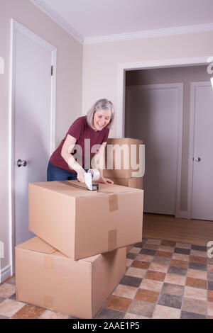 Woman in her early fifties closing a cardboard box with tape for moving it to other house Stock Photo
