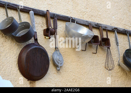 Vintage or Antique Collection of Old Kitchen Utensils Hanging on Wall Rack including Pans, Drainers & Spatulas Stock Photo