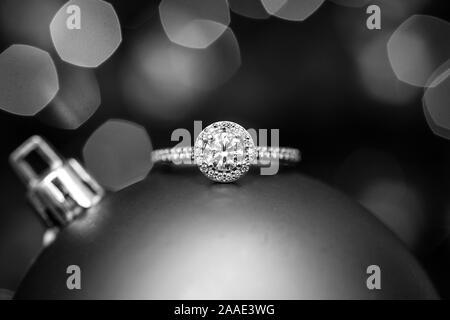 Engagement ring on a Christmas ornament with lights in the background. Black and white. Stock Photo