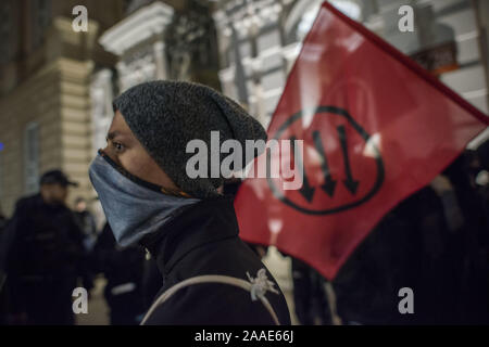 Warsaw, Mazowieckie, Poland. 20th Nov, 2019. A masked anti-fascist student seen next to the Antifa flag during the protest.Anti-Fascists students and activists from Warsaw University gathered under the slogan Here we learn, we do not Hail (a nazi gesture greeting Hitler), blocking the gates to the campus from a group of Nationalists, who wanted to hold a so called protest of leftists supporting immigrant students and the indoctrination of Polish students by LGBTQ lobby. Credit: Attila Husejnow/SOPA Images/ZUMA Wire/Alamy Live News Stock Photo