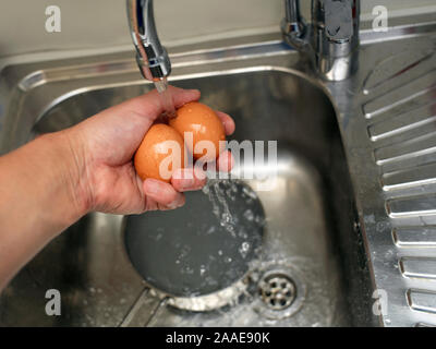 A kitchen sink and a hand holding  boiled eggs under cold water, indoor close-up Stock Photo