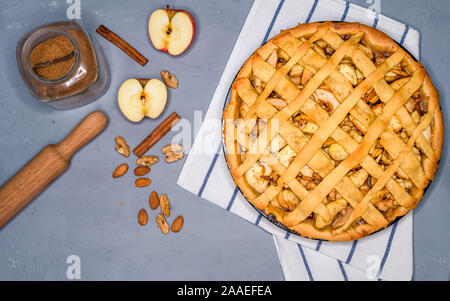 apple pie on a gray kitchen towel, with apples, cinnamon, sugar and nuts, top view Stock Photo