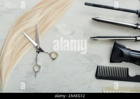 Flat lay composition with Hairdresser tools, scissors and strand of blonde hair: scissors, combs, hair iron on gray background. Hairdresser service Stock Photo
