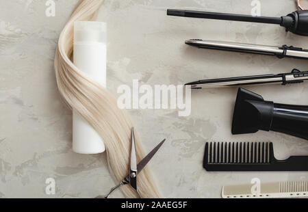 Flat lay composition with Hairdresser tools and white bottle of cosmetic product, blonde hair on gray background. Shampoo mockup. Space for design Stock Photo