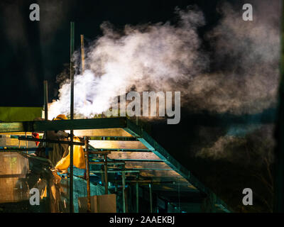 SINGAPORE - 9 JUNE 2019 - Construction worker in performs metal welding work at a building site for at night, creating a diagonal plume of smoke. With Stock Photo