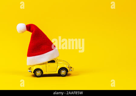 Vilnius, Lithuania - November 16, 2019: Little retro toy model car with small red Christmas Santa Claus hat on yellow background Stock Photo