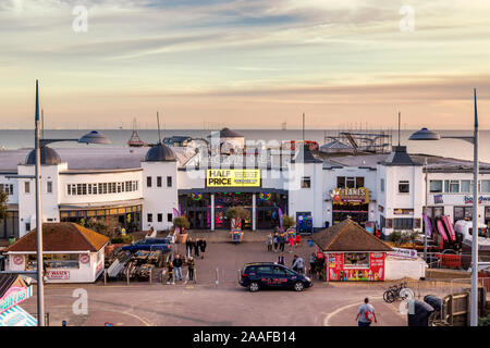 The facade of Clacton Pier with visitors in the foreground and the wind turbines of Gunfleet Sands offshore wind farm in the North Sea behind. Stock Photo