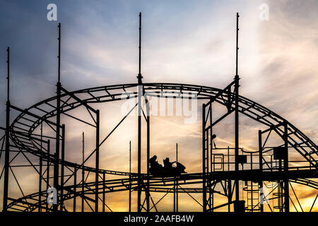 Silhouette of people riding a roller coaster, set against a beautiful golden sky. Stock Photo