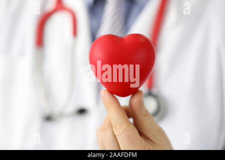 Doctor hold in hand red toy hert against hospital Stock Photo