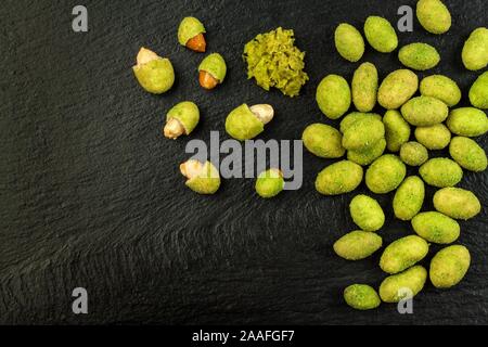 Wasabi Coated Peanuts on slate board. Japanese Wasabi Spice. Green wasabi peanuts on a black plate on a dark background. Stock Photo