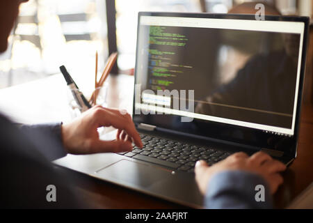 Back view over the shoulder shot of developer programmer with laptop. Program code and script data on the screen. Young freelancer in glasses working Stock Photo