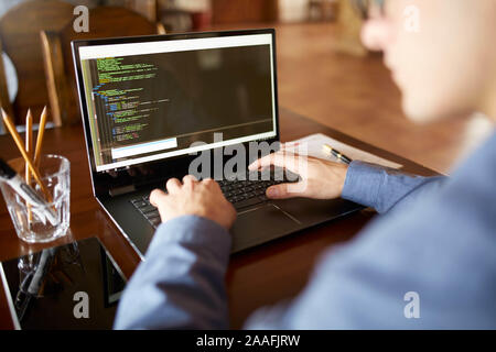 Back view over the shoulder shot of developer programmer with laptop. Program code and script data on the screen. Young freelancer in glasses working Stock Photo