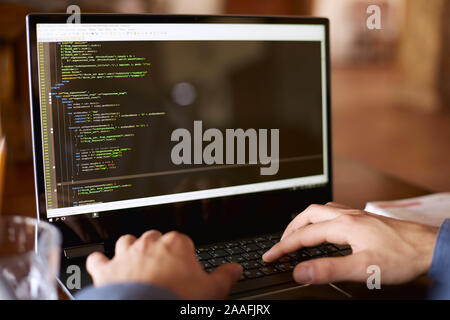 Back view over the shoulder shot of developer programmer with laptop. Program code and script data on the screen. Young freelancer in glasses working Stock Photo