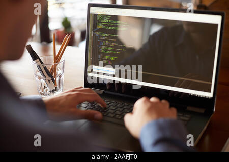 Back view over the shoulder shot of developer programmer with laptop. Program code and script data on the screen. Young freelancer in glasses working Stock Photo