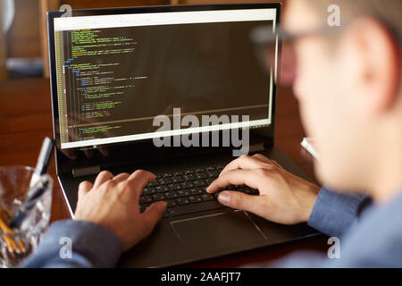 Back view over the shoulder shot of developer programmer with laptop. Program code and script data on the screen. Young freelancer in glasses working Stock Photo