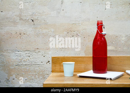 Close-up of a red water bottle and glass on a restaurant table against a light stone wall Stock Photo
