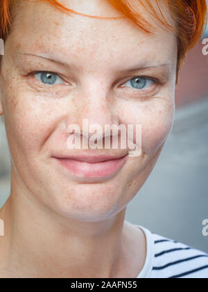 Close-up portrait of a middle-aged red-haired woman looking at the camera and smiling on a blurred street background, selective focus Stock Photo