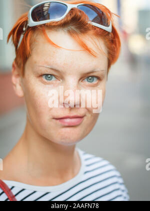 Close-up portrait of a middle-aged red-haired woman looking at the camera and smiling on a blurred street background, selective focus Stock Photo